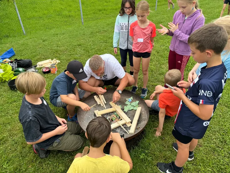 Kinder und Betreuer bauen gemeinsam an einer Feuerschale im Gras
