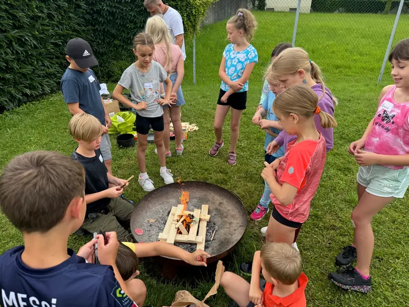 Gruppe Kinder steht im Kreis um eine Feuerschale im Gras