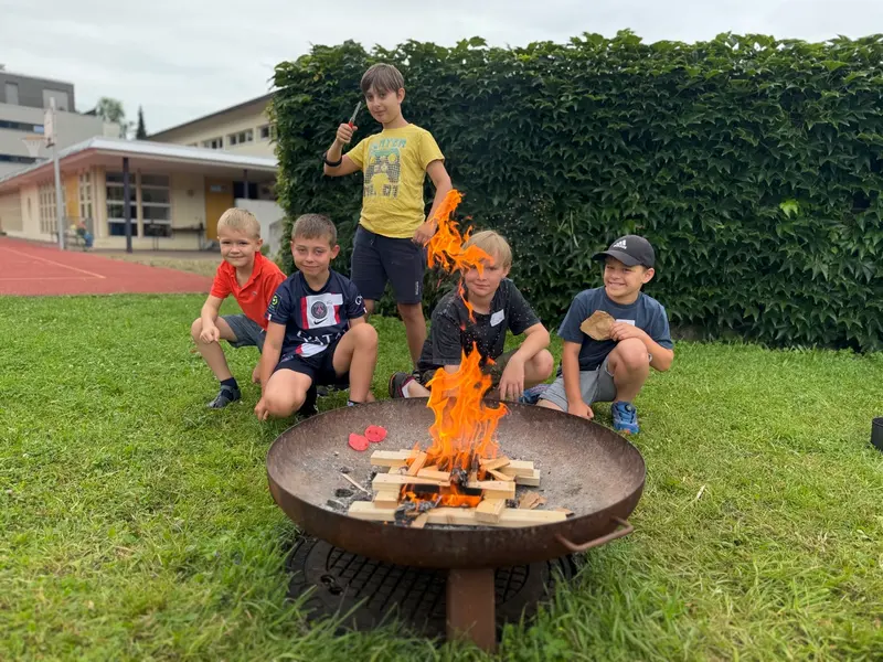 Kinder sitzen und stehen um ein brennendes Feuer im Gras
