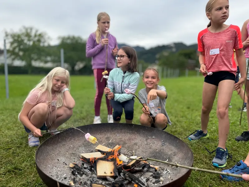 Kinder halten Stöcke über eine brennende Feuerschale im Freien