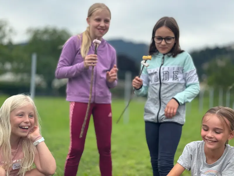 Zwei Kinder halten Stöcke mit Stockbrot vor grüner Wiese
