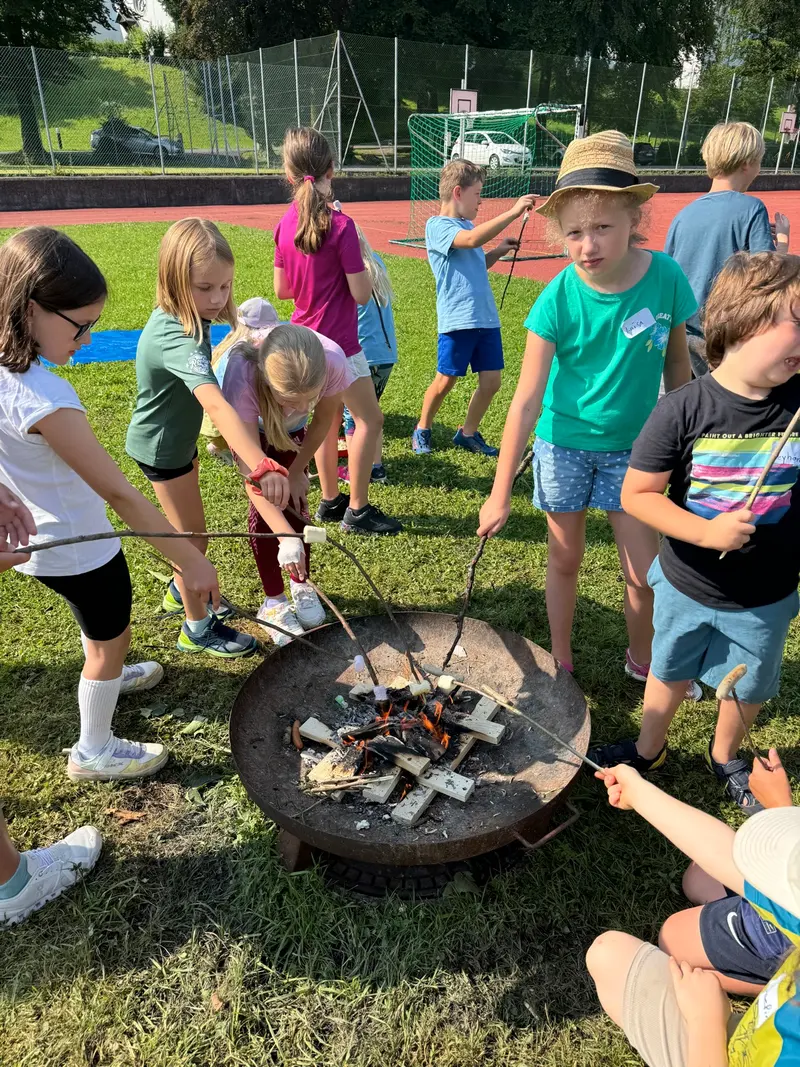 Gruppe Kinder steht um eine Feuerschale und röstet Stöcke