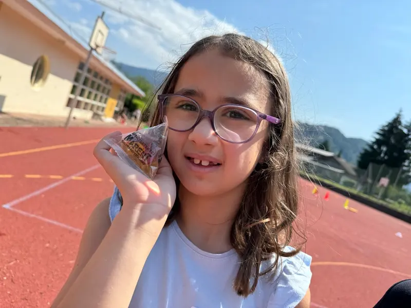 Kind mit Brille hält eine eingepackte Süßigkeit im Freien