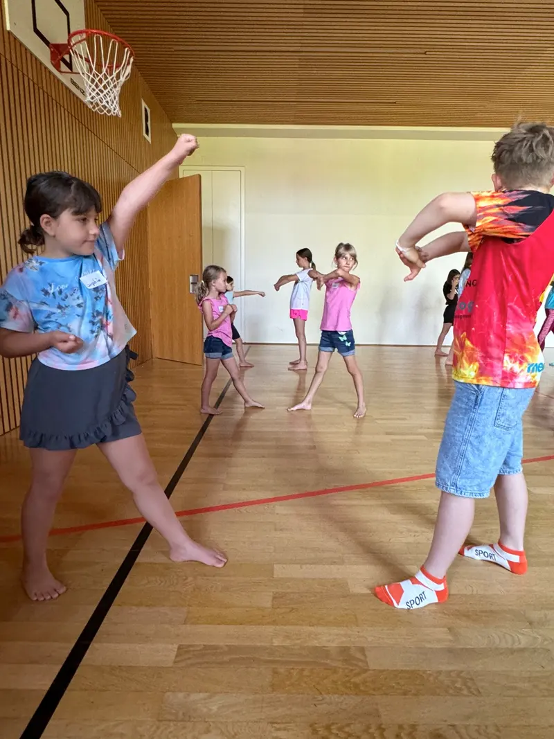 Gruppe Kinder tanzt mit erhobenen Armen in der Turnhalle