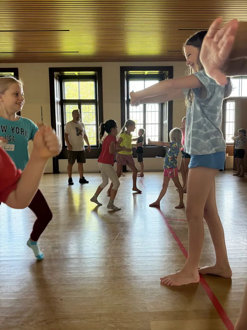 Kinder machen unter Aufsicht eine Dehnübung in der Turnhalle