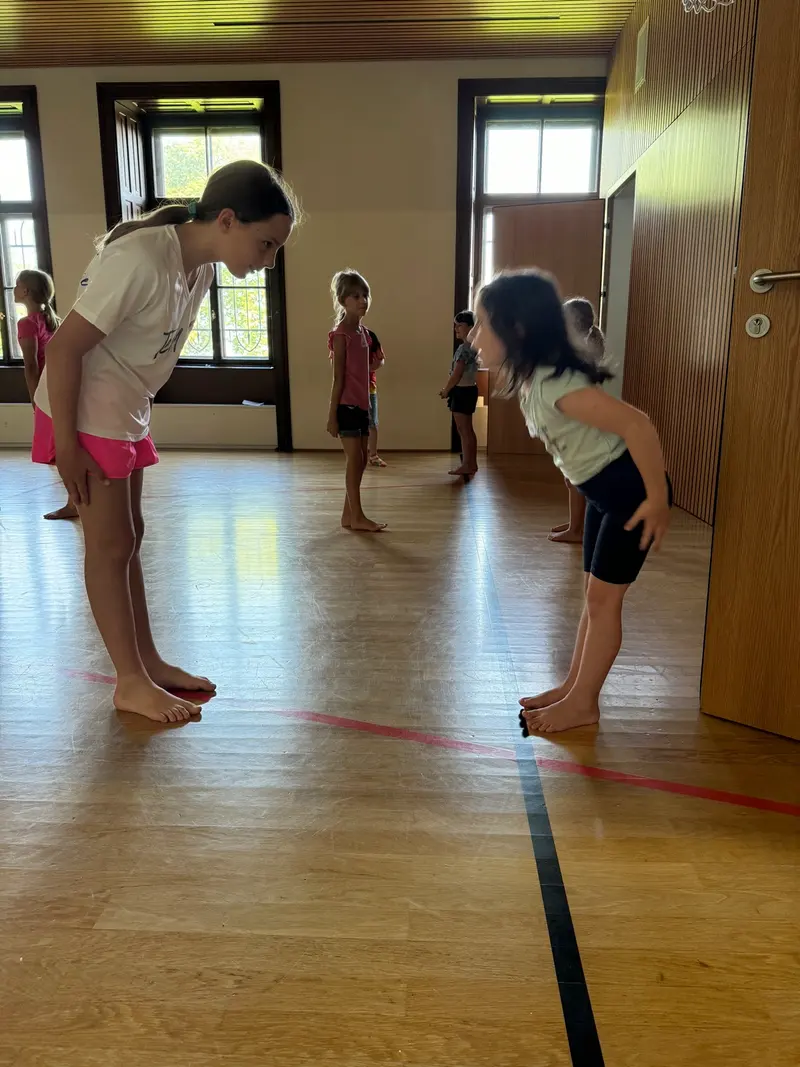 Zwei Kinder üben barfuß eine Turnübung auf dem Hallenboden