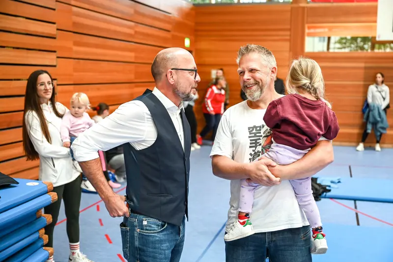 Zwei Männer im Gespräch, einer trägt ein Kleinkind