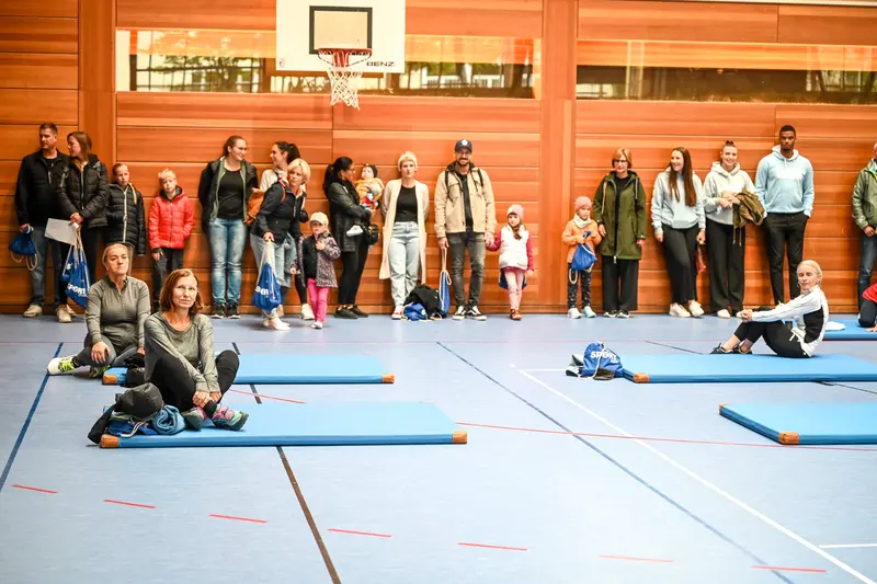 Zuschauer stehen an der Hallenwand, Turnmatten am Boden