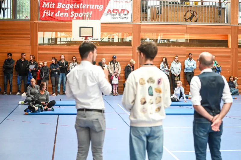 Drei Personen stehen vor Publikum an der Hallenwand