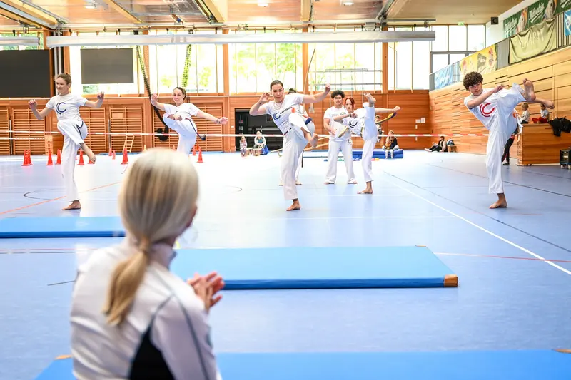 Capoeira-Gruppe übt hohe Tritte, Person klatscht im Vordergrund