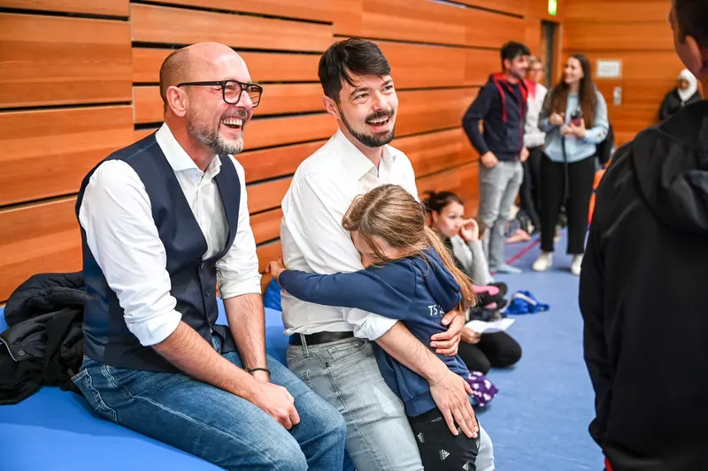 Zwei Männer lachen, einer trägt ein Kind im Arm