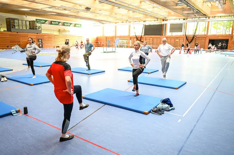 Personen turnen auf blauen Matten in der Sporthalle