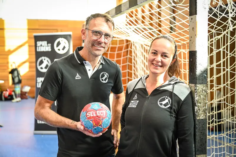 Zwei Personen posieren mit einem Handball vor einem Tor