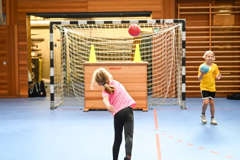 Kind im pinken Trikot wirft Ball auf Torwand