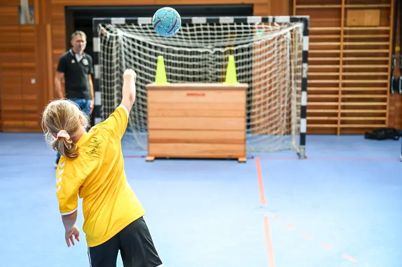 Kind im gelben Trikot wirft Ball auf Torwand