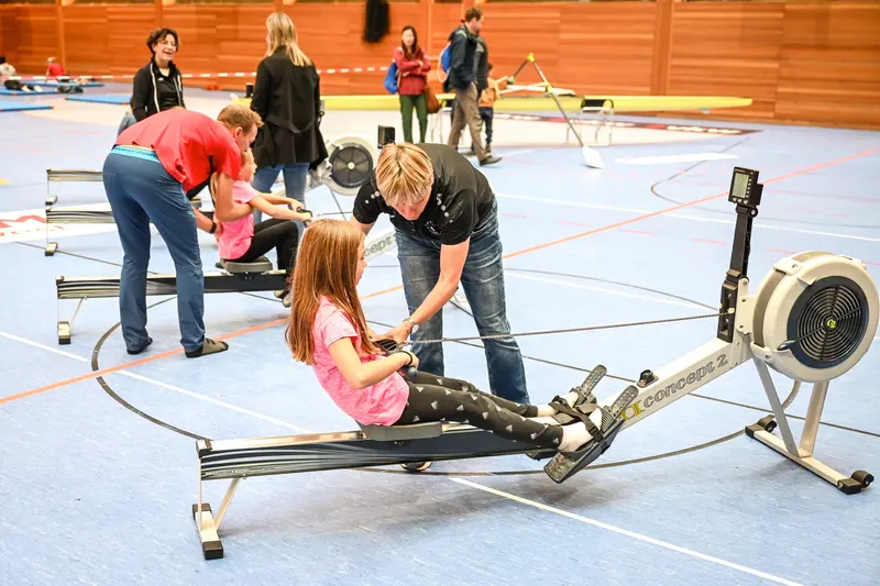Erwachsene helfen Kind beim Training am Rudergerät