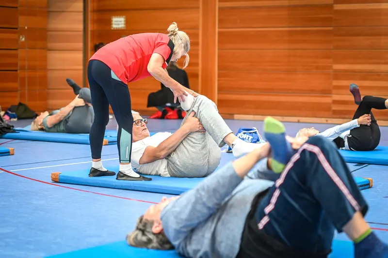 Trainerin dehnt die Beine einer liegenden Person