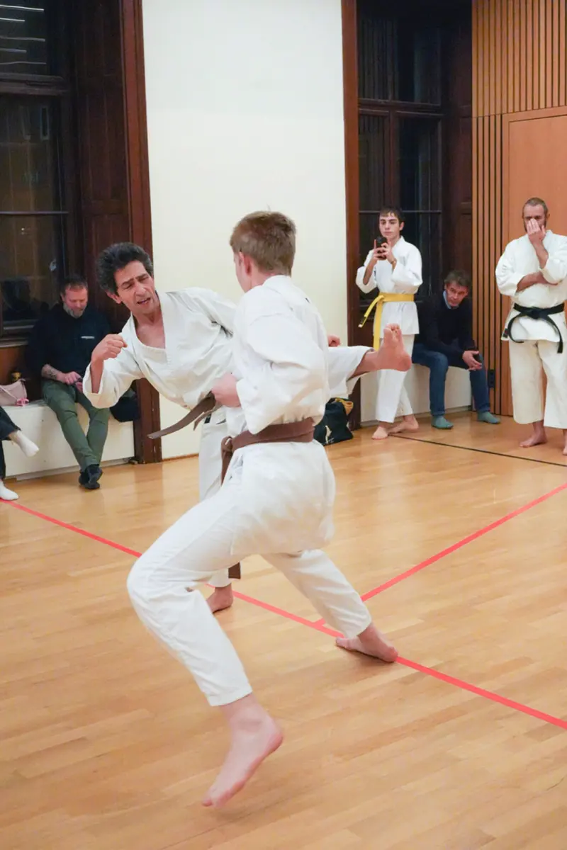 Zwei Personen üben Kumite, im Hintergrund sitzt ein Kind