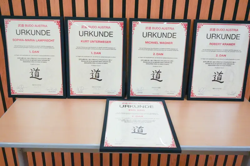 Vier gerahmte Urkunden hängen an der Wand, eine liegt auf dem Tisch