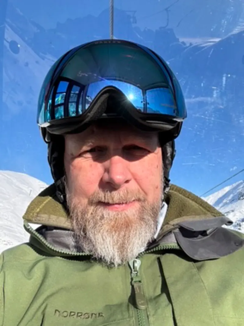 Person mit Skibrille und Helm lächelt vor verschneiten Bergen