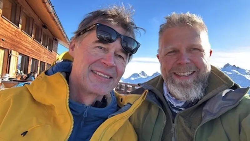 Zwei Personen mit Sonnenbrille lächeln vor Häusern im Schnee