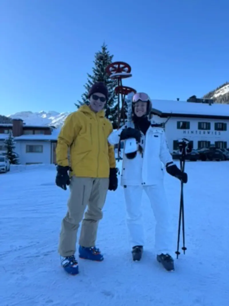 Zwei Personen in Skikleidung stehen vor einem Haus im Schnee