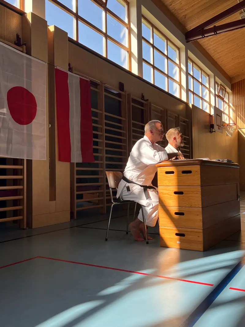 Person sitzt am Prüfertisch vor österreichischer und japanischer Flagge.