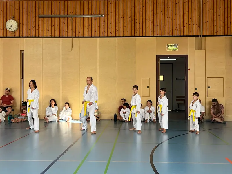 Kinder in Karategi stehen in einer Reihe vor Zuschauern.