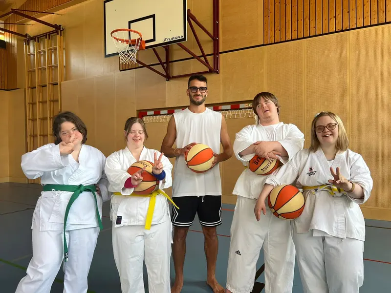 Fünf Personen im Karategi halten Basketbälle unter einem Basketballkorb