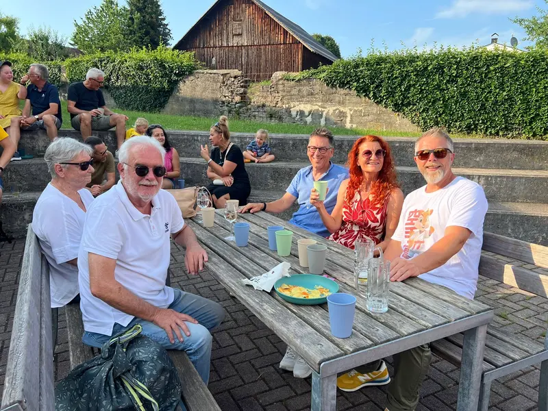 Gruppe sitzt gemeinsam an Holztisch im Garten