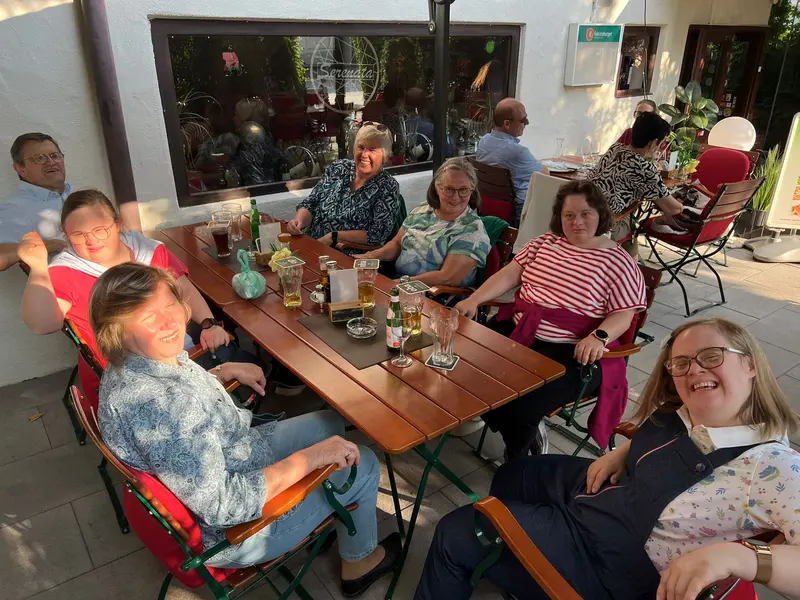 Gruppe sitzt gemeinsam an langem Tisch auf Terrasse