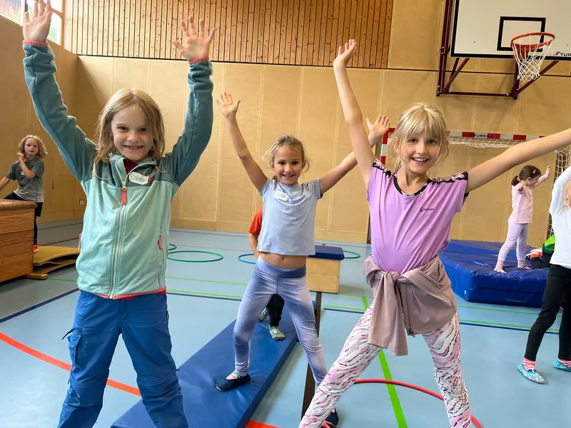 Drei Kinder springen mit erhobenen Armen in der Turnhalle