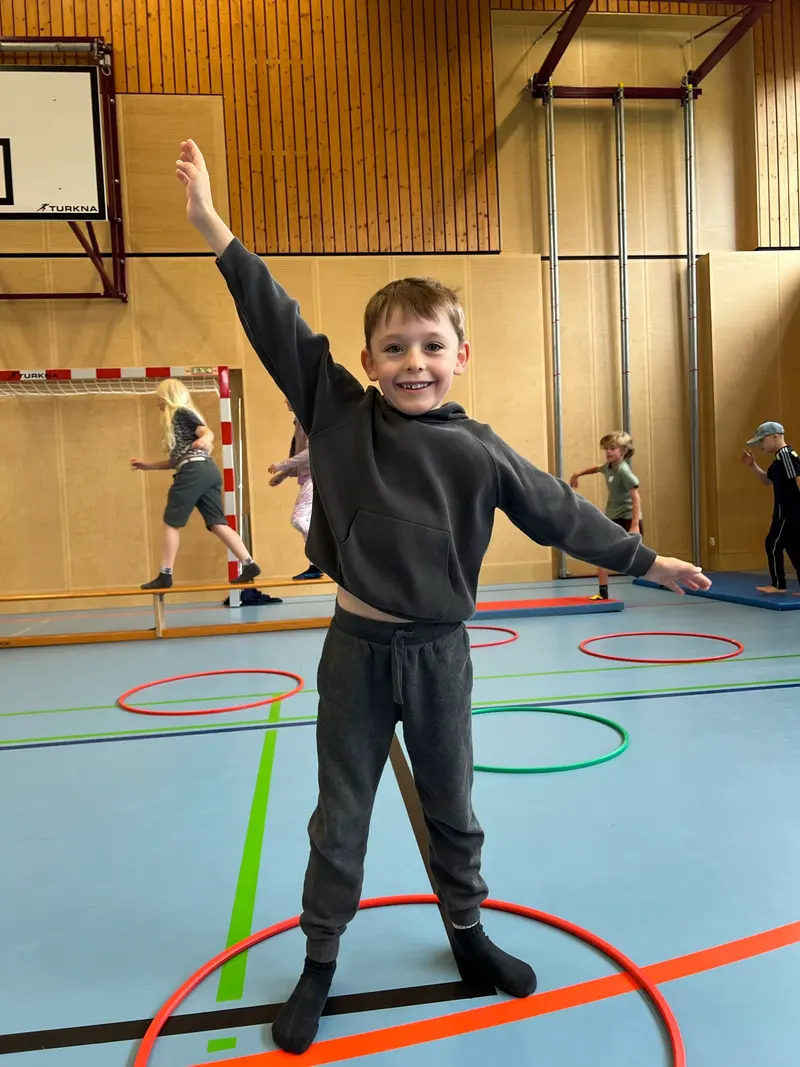 Kind steht mit ausgestreckten Armen zwischen Hula-Hoop-Reifen in der Turnhalle