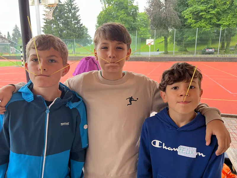 Drei Kinder stehen Arm in Arm auf dem Sportplatz