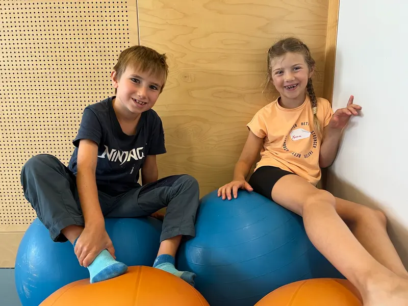 Zwei Kinder sitzen lachend auf großen Gymnastikbällen