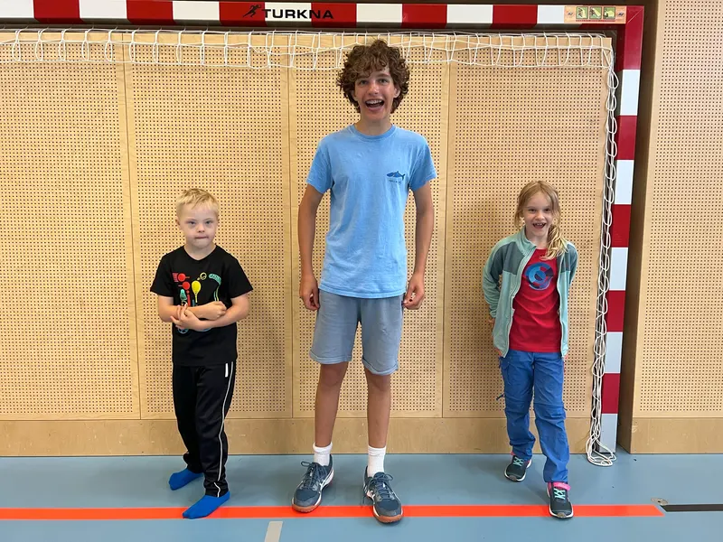 Drei Kinder unterschiedlicher Größe stehen nebeneinander in der Turnhalle