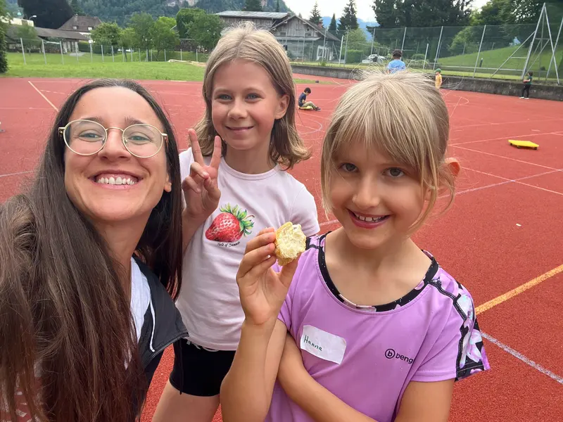 Betreuer und zwei Kinder lächeln, ein Kind hält Gebäck