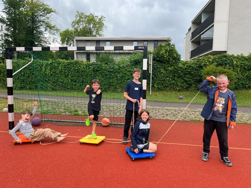 Kinder ziehen sich auf Rollbrettern über den Sportplatz