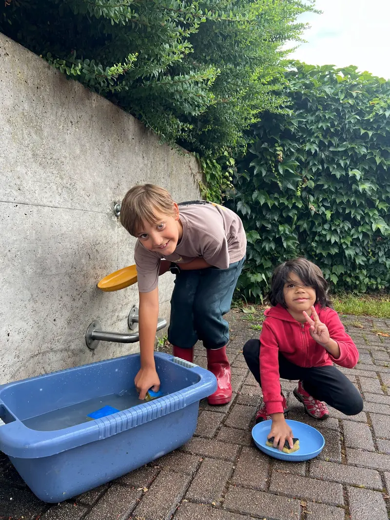 Zwei Kinder füllen an einer Wasserstelle im Freien eine Wanne