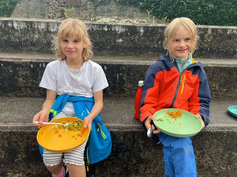 Zwei Kinder sitzen auf Stufen und essen von gelben Tellern