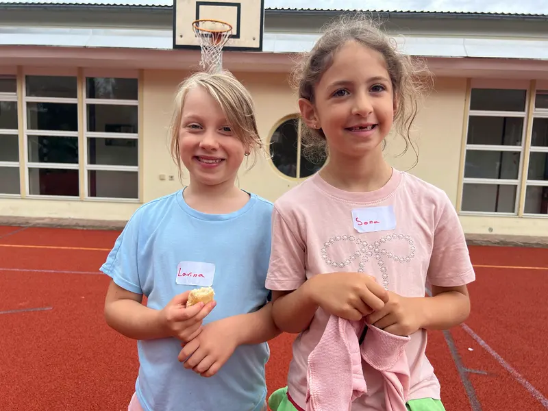 Zwei Kinder stehen lächelnd nebeneinander auf dem Sportplatz