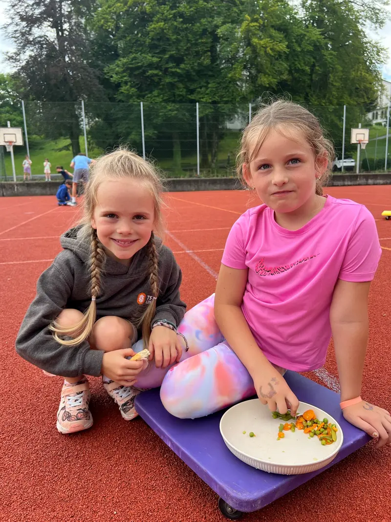 Zwei Kinder sitzen lächelnd auf dem Sportplatz
