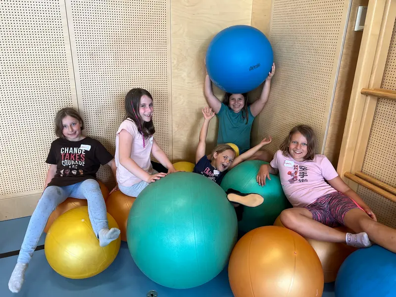Gruppe von Kindern sitzt und liegt auf bunten Gymnastikbällen