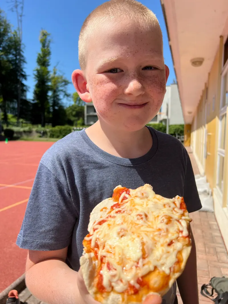 Kind isst herzhaft ein Stück Pizza im Freien