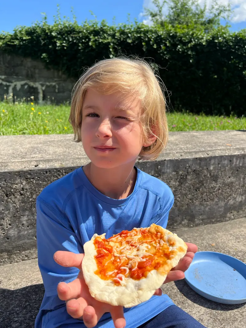 Kind hält ein Stück selbstgemachte Pizza in den Händen