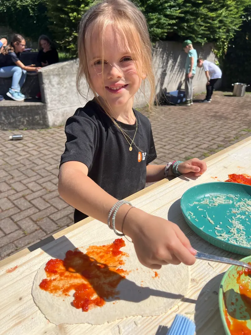 Kind bestreicht einen Teigfladen mit Tomatensauce