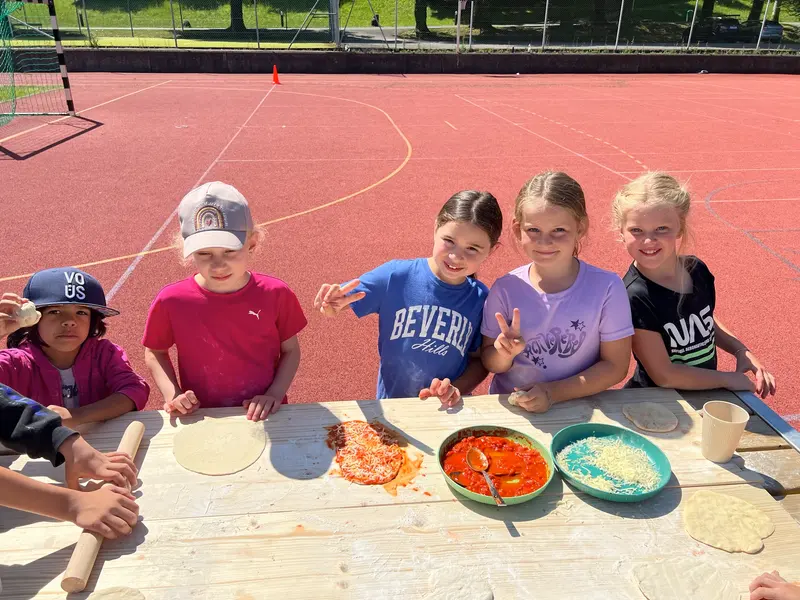 Gruppe von Kindern sitzt am Tisch beim Pizzabelegen