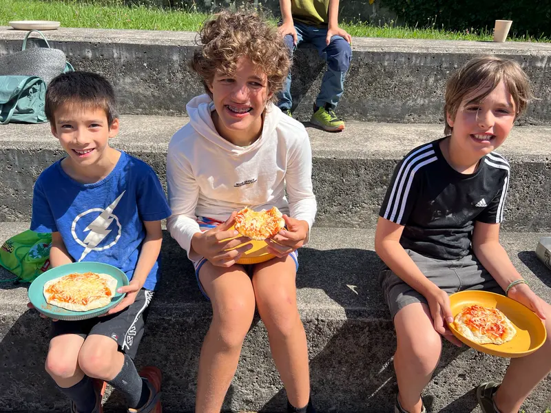 Drei Kinder sitzen mit Pizzastücken auf einer Treppe