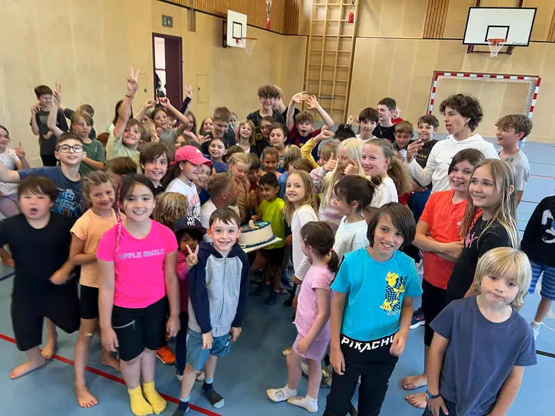 Große Gruppe von Kindern posiert winkend in der Turnhalle
