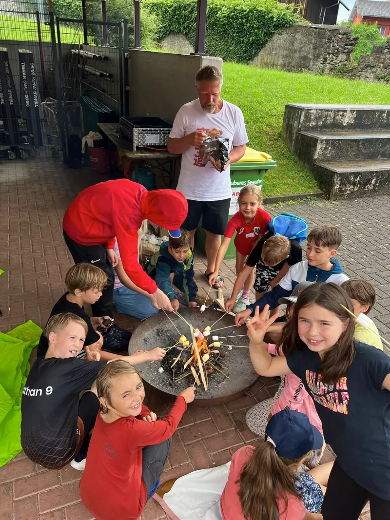 Kinder rösten mit Betreuern Marshmallows über einer Feuerschale